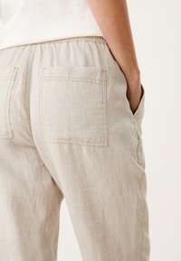 Beige linnebyxor med elastisk midja, med två påsydda fickor bak och en mjuk, strukturerad yta.