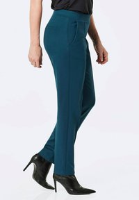Teal op maat gemaakte broeken met een hoge tailleband, zijzakken en een rechte pijp pasvorm. Gecombineerd met zwarte hoge hakken voor een formele uitstraling.