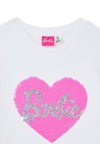 T-shirt bianco in cotone con un grande design a cuore di paillettes rosa, con la parola "Barbie" in paillettes argentate al centro.