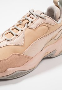 Baskets en cuir beige avec des accents en daim, des superpositions texturées et des lacets gris clair. Dotées d'une semelle épaisse avec un design ondulé.