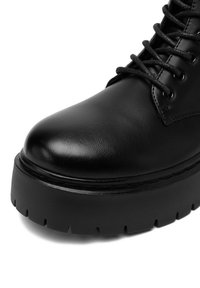 Melna ādas potītes zāle ar noapaļotu purngalu, biezu platformas zoli un šņorējamu priekšpusi. Uztverams teksturēts materiāls un smalki šuvumi.