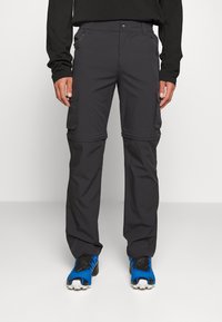Pantalon cargo gris avec poches zippées, fabriqué en tissu léger, avec une coupe droite. Associé à des chaussures de sport bleues.