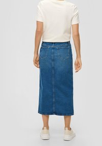 Modrá džínová midi sukně s kapsami vzadu, rovný střih a délka pod kolena. Kombinováno s bílým topem s krátkým rukávem a světlými teniskami.