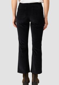 Pantalones de pana negra acampanados con bolsillos traseros, que presentan una textura suave y una cintura ajustada, combinados con botas de tobillo marrones.