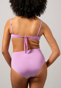 Högmidjad bikini i mjukt lavendelfärgat tyg, med tunna justerbara remmar och en knytning på ryggen. Slät textur med minimala sömmar.