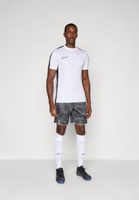 Nike sportswear sæt bestående af en hvid kortærmet top, sorte sideakcenter, shorts med sort og grå mønster, hvide sokker og sorte fodboldstøvler.