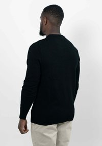 Zwarte trui met lange mouwen en een ronde hals, gemaakt van een gladde stof. Getoond vanuit de achterkant, met een rechte snit en geribbelde zoom.