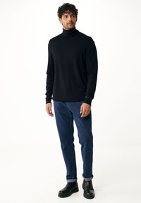 Zwarte turtleneck trui met lange mouwen, aansluitend ontwerp. Gecombineerd met blauwe denim jeans en zwarte stevige enkelboots. Minimalistische benadering.
