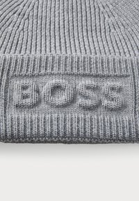 Szürke kötött sapka bordás textúrával, elöl feltűnő "BOSS" logóval. Az anyaga lágy és melegnek tűnik.