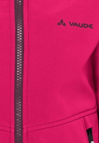 Fuchsia jas van textiel met een structuur, voorzien van een zichtbare donkere rits en een bedrukte logo op de bovenste linkerzijde. Inclusief zakken aan de zijkanten.