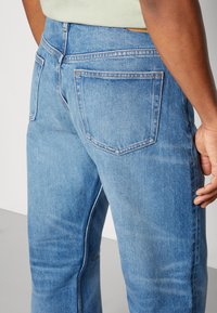 Jeans in denim azzurro chiaro con una vestibilità dritta, dotati di tasche posteriori, sottili segni di usura e cuciture a contrasto lungo le cuciture.