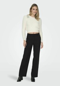 White cropped sweater with a fluffy texture and decorative accents on shoulders, paired with high-waisted black wide-leg trousers and ankle boots.