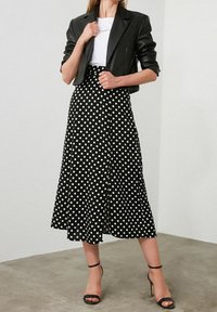 Falda midi de lunares en blanco y negro de tela ligera, combinada con una chaqueta negra ajustada y cropped y tacones negros con tiras.
