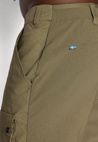 Pantaloni cargo verde oliva realizzati in tessuto testurizzato, dotati di tasche laterali e una piccola bandiera svedese ricamata sopra la tasca posteriore.