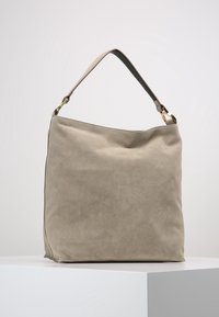 Grote, zachte beige suède tas met een enkele verstelbare leren riem en goudkleurige metalen accenten, met een eenvoudig, onopgesmukt ontwerp.