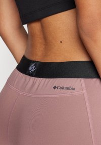 Visoke tajice od mekane ružičaste tkanine s crnim elastičnim pojasom koji sadrži Columbia logo i suptilne šivane detalje.