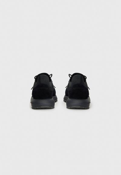 Black athletic shoes with a smooth fabric upper and suede accents. Features a low heel and textured rubber outsole. Laces and heel pull tabs.