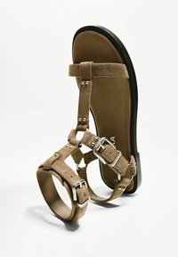 Bruna mocka sandaletter med flera remmar, silverfärgade spännen och en platt svart sula. Designen framhäver en minimalistisk, öppen tå-stil.