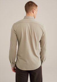 Cămașă lungă cu mâneci, de culoare bej deschis, cu guler, textură netedă și mansete cu nasturi. Linia de jos curbată, croială ajustată și design minimalistic.