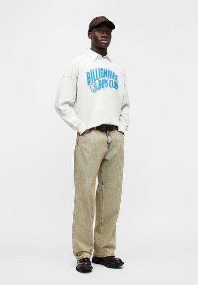 Γκρι υπερμεγέθη φούτερ με μπλε λογότυπο "Billionaire Boys Club", μπεζ ριγέ φαρδιά παντελόνια, καφέ καπέλο και σκούρα παπούτσια.
