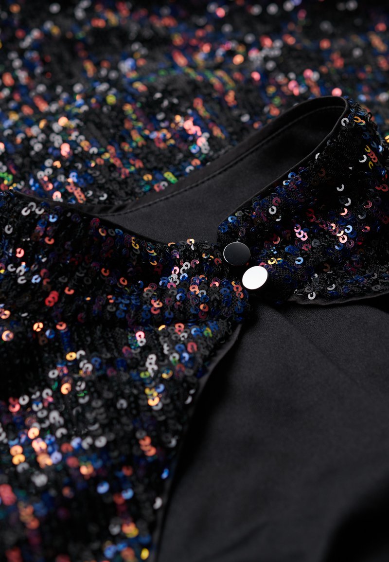 Czarna bluzka z tkaniny ozdobiona wielokolorowymi cekinami, charakteryzująca się gładką teksturą i kołnierzykiem z dwoma czarnymi guzikami blisko dekoltu.