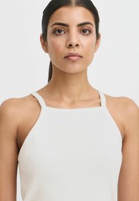 Top de tirantes rectos blanco con escote cuadrado. La tela tiene una textura suave y se ajusta estrechamente alrededor de la parte superior del cuerpo.