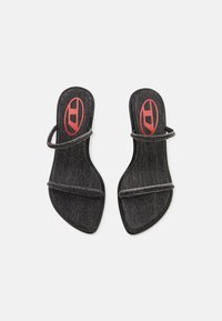 Sandale cu toc din denim negru, cu două curele subțiri și vârf ascuțit. Prezintă un logo roșu pe talpă și cusături în contrast pe margini.