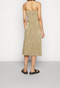 Béžové midi šaty s tenkými ramínky, se vzorem vyraženého loga a hladkým povrchem. V kombinaci s černými plochými sandály.