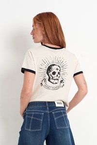 Kermakoska t-paita mustalla rengaskravaattorilla, jossa on pääkallo grafiikka ja teksti "UNHOLY THREADS". Yhdistetty farkkuihin, takanäkymä.