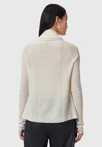 Ljust beige ribbad cardigan med hög krage, sänkta axelsömmar och avslappnad passform, med vertikala stickmönster och sidov slit.