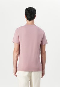 Tricou cu mâneci scurte din bumbac roz pal, cu guler rotund. Dispune de o textură simplă și netedă și o croială clasică. Fără logo-uri vizibile.