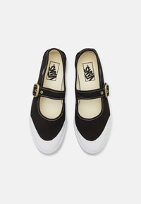 Baskets noires style Mary Jane avec embouts et semelles en caoutchouc blanc, dotées de brides réglables à boucle et de semelles intérieures avec logo Vans.