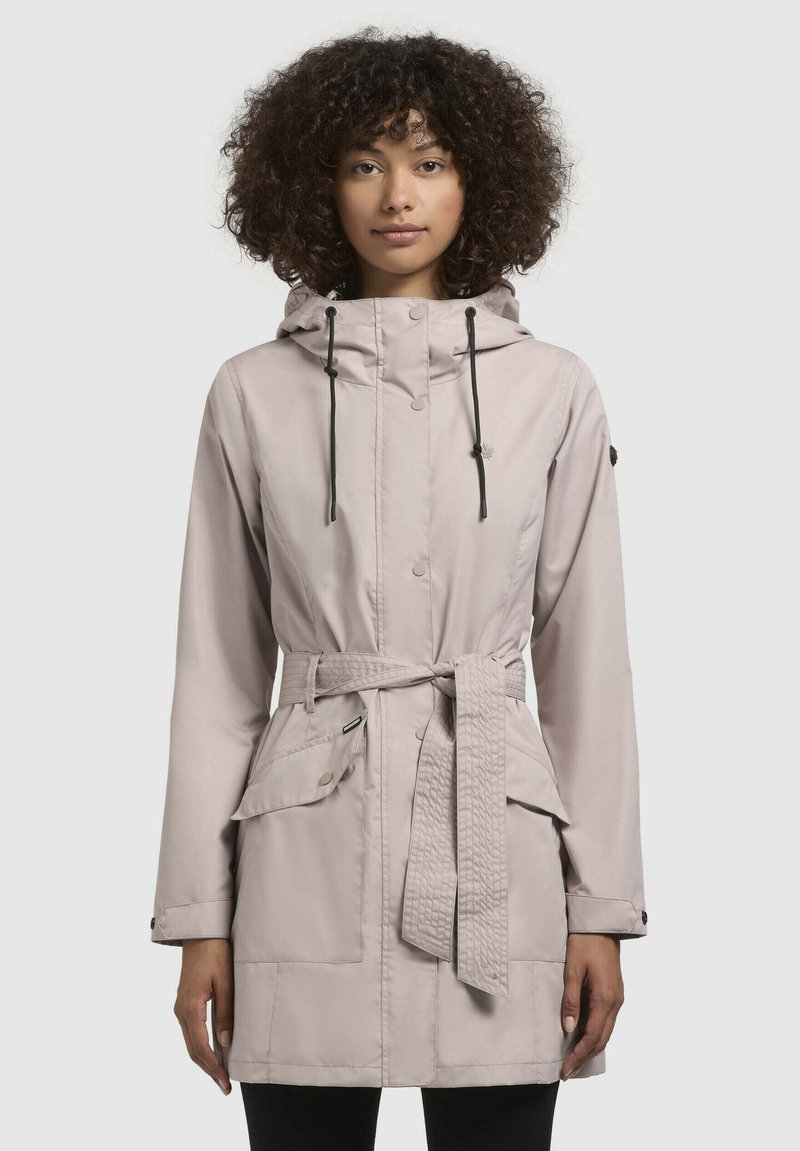 Parka imperméable beige clair avec taille cintrée, capuche et deux poches avant. Équipée de cordons de serrage à bascule et d'une finition lisse et texturée.