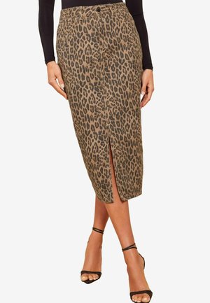 Kokerrok met luipaardprint tot op de knie, met een split aan de voorkant, gedragen met een zwarte top met lange mouwen en zwarte sandalen met hoge hakken en enkelbandje.