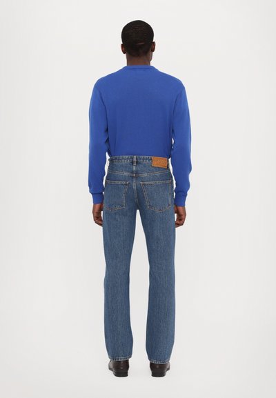 Blue long-sleeve top with round neckline paired with classic denim jeans, featuring a straight-leg cut and a branded leather patch on the back.