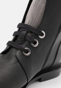 Czarny skórzany botek na kostkę z teksturowanym wykończeniem, szarym siateczkowym panelem, srebrnymi oczkami i czarnymi sznurówkami. Niski, złoty obcas.