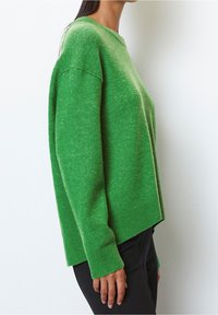 Vihreä villaneule rentoa istuvuutta, ribbaus hihansuissa ja helmassa. Ominaisuuksiin kuuluu pyöreä kaula-aukko ja hieman pidempi takapään helma.