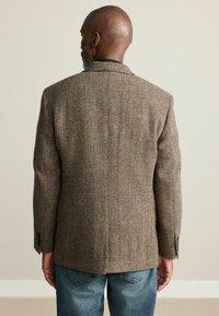 Brown tweed blazer with a houndstooth pattern, single vent, and notched lapels, paired with blue denim jeans, view from the back.