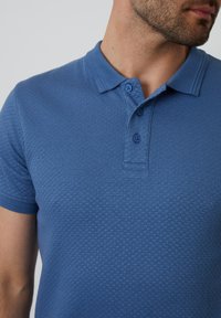 Modrá texturovaná polo košile s třemi knoflíky a plochým límcem. Krátké rukávy, vyrobená z měkkého materiálu.