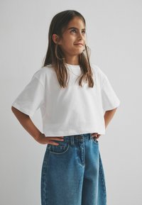 Weißes kurzärmliges, cropped T-Shirt, kombiniert mit locker sitzenden blauen Jeans aus Denim, die sichtbare Nähte und Vordertaschen aufweisen.