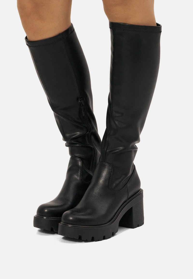 Botas negras hasta la rodilla hechas de cuero suave, con una suela de plataforma gruesa y tacón bloque, y un cierre de cremallera lateral para un fácil poner y quitar.