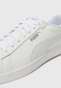 Bijele tenisice s gornjištem od glatke kože, sa uloškom za gležnjeve, bijelim vezicama i svijetlosivim detaljima. PUMA logo u ružičastom zlatu.