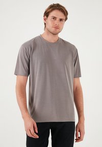 Tricou scurt gri, cu mânecă scurtă, fabricat dintr-un material neted și ușor. Are un guler rotund și o croială lejeră, fără modele vizibile.