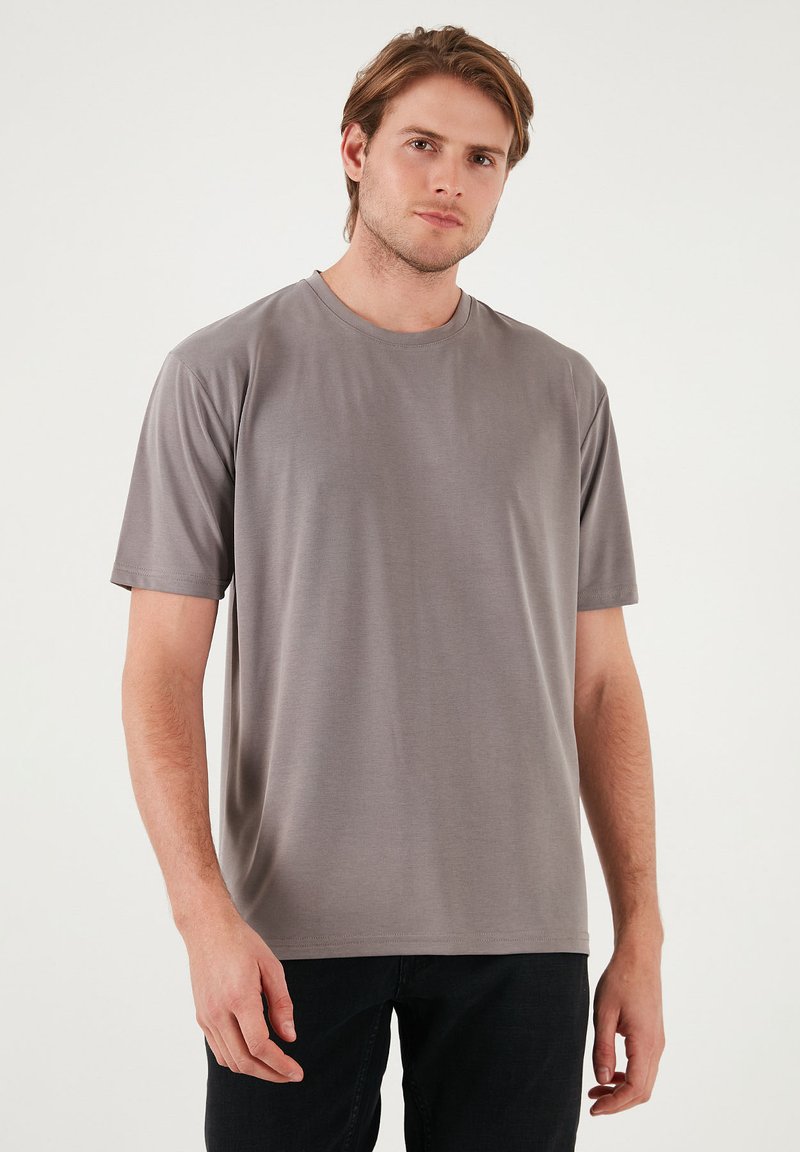 Tricou scurt gri, cu mânecă scurtă, fabricat dintr-un material neted și ușor. Are un guler rotund și o croială lejeră, fără modele vizibile.