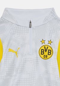 Valge ja kollane spordijakke neljandiku tõmblukuga, millel on Puma logo, tekstuurne muster ja Borussia Dortmundi vapp koos kahe tähisega.