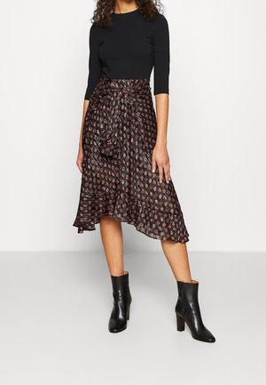 Sort langærmet top parret med en flowy sort nederdel med røde og hvide geometriske mønstre. Sættet afsluttes med sorte hælede ankle boots.