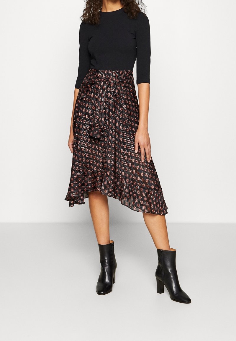 Czarna bluzka z długim rękawem zestawiona z luźną czarną spódnicą z czerwonymi i białymi wzorami geometrycznymi. Całość dopełniają czarne botki na obcasie.