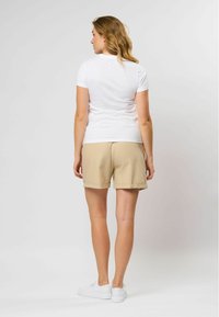 Witte T-shirt met korte mouwen, gecombineerd met beige shorts, met een losse pasvorm en rechte zoom. Model draagt witte sneakers.