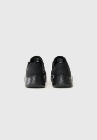 Chaussures de sport noires avec un dessus texturé, des talons arrondis et une semelle en caoutchouc lisse ; le design présente un motif géométrique subtil.