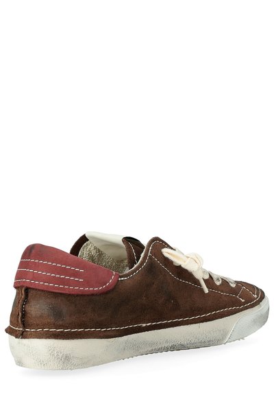 Sneakers in suede marrone con una linguetta rossa sul tallone, lacci beige e suola in gomma bianca. Dettagli di cucitura evidenti lungo il bordo.